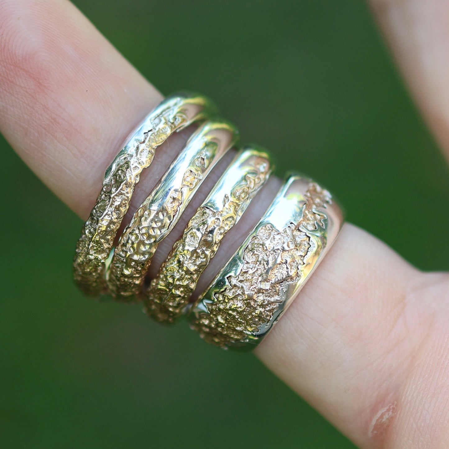 Gold ring with textured design on a finger against a blurred green background