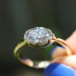 Gold ring with a large diamond held by a hand with blue nail polish against a blurred background