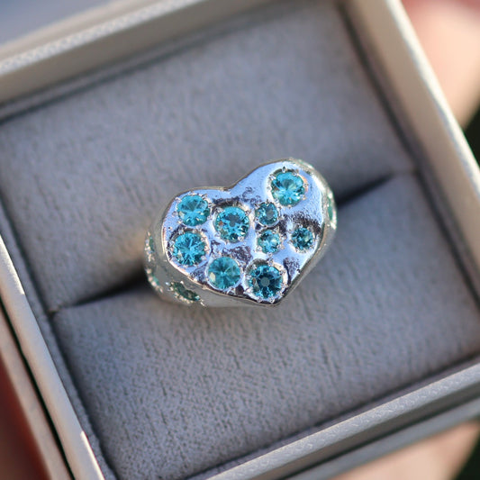 Heart-shaped silver charm with blue gemstones in a box
