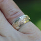 Gold and silver ring on a finger with a blurred green background