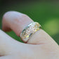 Gold ring with a textured band worn on a finger against a blurred green background