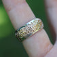 Silver and gold ring on a finger with a blurred green background