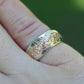 Gold and silver ring on a finger with a blurred green background