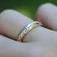 Gold ring with small diamonds on a finger against a blurred green background