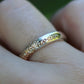 Gold ring with diamond accents on a finger against a blurred green background