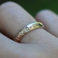 Gold ring with small diamonds on a finger against a blurred green background