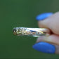 Gold ring held by a hand with blue nail polish against a blurred green background