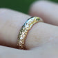 Gold ring with a textured design on a finger against a blurred green background