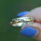 Silver ring with intricate design held by a hand with blue nail polish against a blurred green background