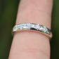 Silver ring with diamonds on a person's finger against a blurred green background
