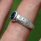 Silver ring with star design and blue stone on a finger against a green background