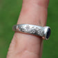 Silver ring with star and moon designs on a finger against a green background