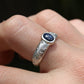 Silver ring with a blue gemstone on a finger against a dark background