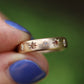 Gold ring with star-shaped diamonds held by a hand with blue nail polish against a blurred green background
