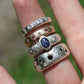 Stack of silver rings with gemstones on a finger against a blurred green background